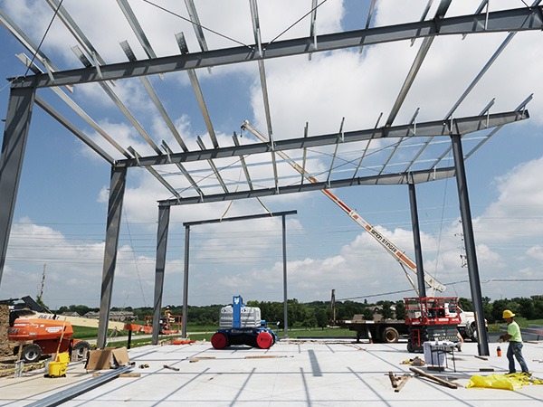 Structural steel frame installation in progress for a pre-engineered metal building, with crane and crew on job site.